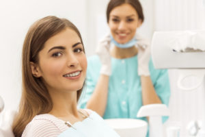 Portrait of a happy patient with braces on the teeth, sitting in the dental chair, in the background a young doctor dentist